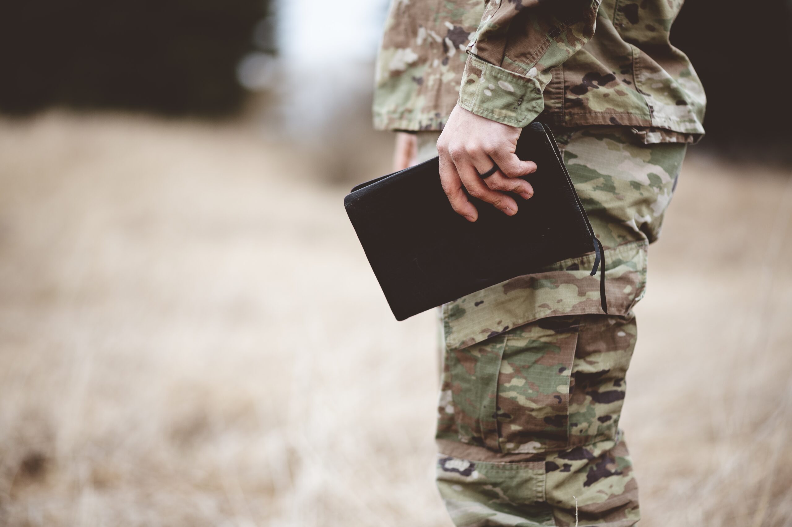 shallow focus shot of a young soldier holding a bible in a field
